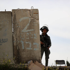 An Israeli soldier wearing helmet stands to the right of a large slab of concrete.