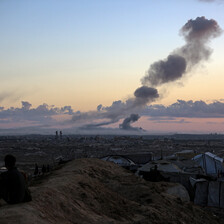 Plumes of dark smoke hover above a sunrise as a man watches.