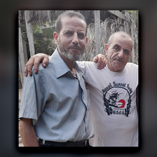 In daytime, two smiling men pose with arms on the other's shoulders.