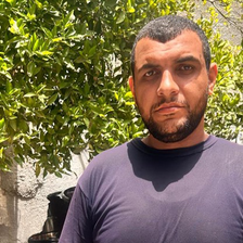 Portrait of a man standing in front of a wall with a tree growing behind it 