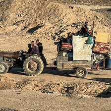 A tractor carries people and belongings along a sandy path