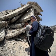 A girl wearing a headscarf and a backpack looks toward the camera while a man stands behind her