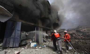 Firefighters aim hose at building billowing with smoke