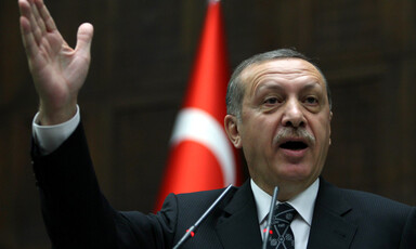 Turkish prime minister seen gesturing with hand in front of flag of Turkey