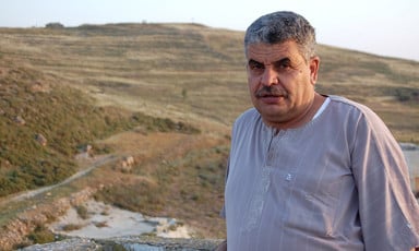 Man stands with Israeli outpost on hill in background