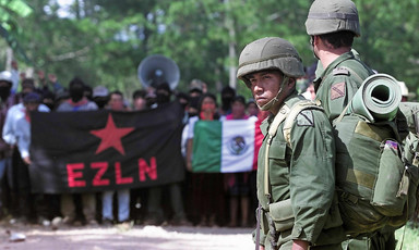 Mexican soldiers stand in front of crowd of protesters holding flags