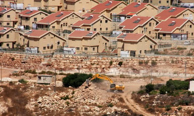 An earth-moving machine works in the foreground with Israeli settlement homes in background