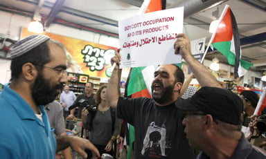 Man holds up sign reading "Boycott occupation and its products" in Arabic and English