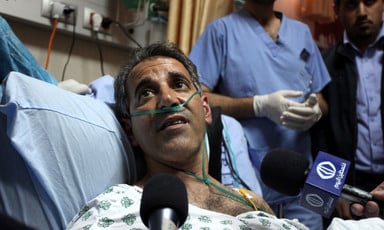 Man on hospital bed surrounded by microphones