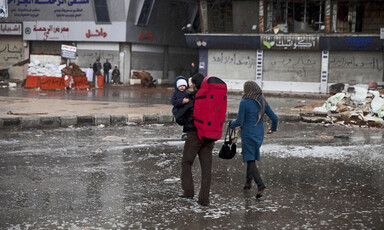 Couple carrying baby cross flooded street in war-torn camp