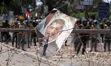 A poster of Mohammed Morsi entangled in barbed wire, with soldiers in background