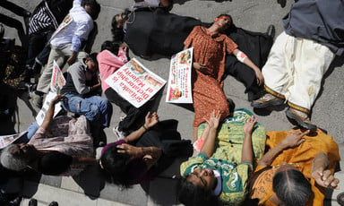 Women wearing mock blood lie on ground surrounded by other seated women