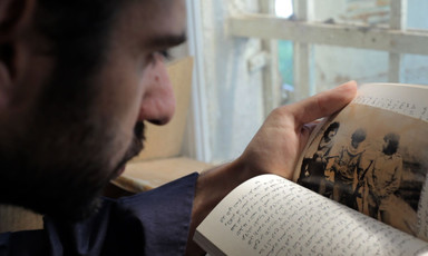 Man looks at Arabic-language book and vintage photograph of armed men