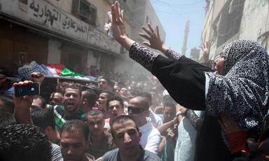 Woman raises her hands above passing funeral procession