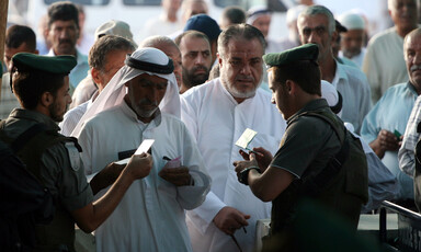 Israeli soldiers inspect the IDs of Palestinian men at a checkpoint