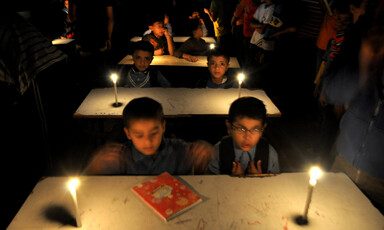 Boys sit at school desks in room lit with candles