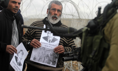 Middle-aged man holds photo of Mandela in front of heavily armed Israeli soldier