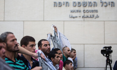 Men wearing checkered scarves hold banners outside court house