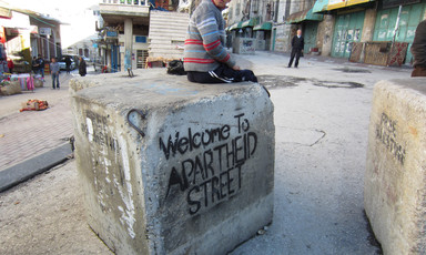 Boy sits on cement block which is spray painted with a stencil reading Welcome to apartheid street