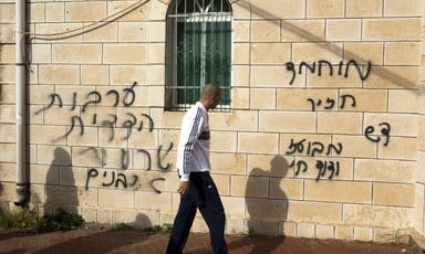 Man walks in front of stone wall spray painted with Hebrew graffiti