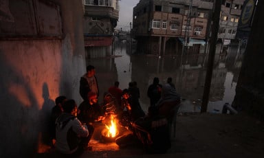 Men sit by campfire in flooded urban area