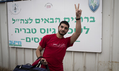 Young man gives carrying duffel bag gives victory gesture with his hand