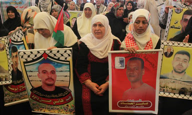 Elderly woman sits amongst crowd holding posters of Palestinian prisoners