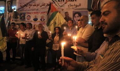 Crowd hold candles in tent covered with posters of political prisoners