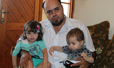Photo shows Amjad Safadi sitting on couch holding two small girls