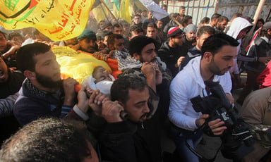 Men carry body of young man wrapped in yellow flag