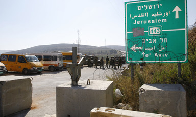 Photo shows highway sign for Route 443 with group of Israeli soldiers forming roadblock in background