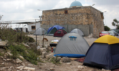 Photograph shows camping tents in front of old church built of stone