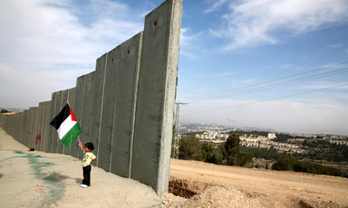Girl holding Palestine flag stands next to section of 25-foot-tall concrete wall under construction