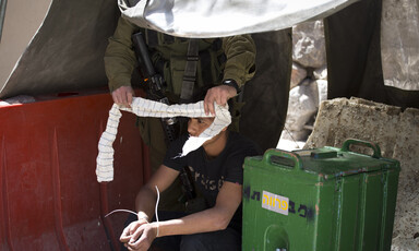 Israeli soldier puts blind fold on zip-cuffed Palestinian youth