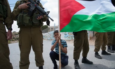 Photo shows boy holding Palestine flag crouching between Israeli soldiers
