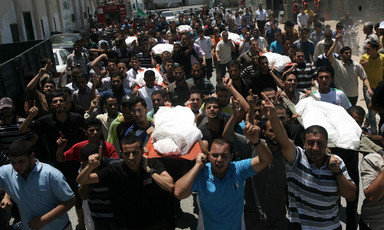 Crowd of men carry shrouded bodies during funeral procession