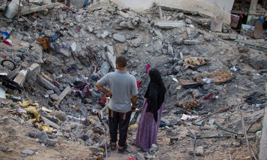Man and woman look at bombed-out crater where home once stood