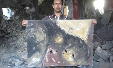 Artist Raed Issa holds up one of his damaged paintings in his bombed-out house in Gaza
