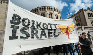 A large banner reading Boikott Israel with an image of a blood-splattered orange slice is held in front of a building