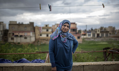 Smiling woman stands underneath clothes line outdoors with buildings and cloudy sky in background