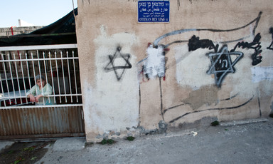 Woman stands behind bars next to walls spray-painted with Stars of David