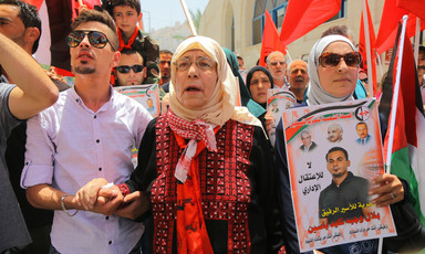 Elderly woman wearing traditional embroidered dress is flanked by two younger relatives at rally