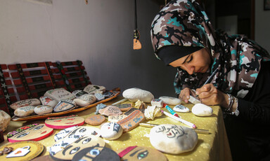 Sitting young woman writes with a pen on a rock while sitting at a table filled with illustrated rocks