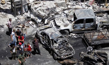 Aerial view of people standing near burnt-out cars and shelled buildings