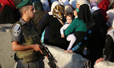 Israeli soldier carrying gun stands in front of queue of women and children at checkpoint