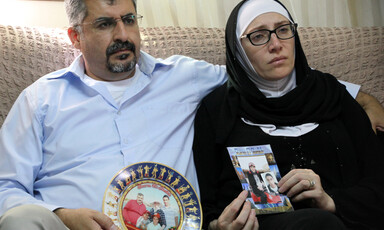 Man and woman sit on couch and hold family photographs