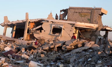 Boys sit on top of rubble in front of destroyed Gaza home