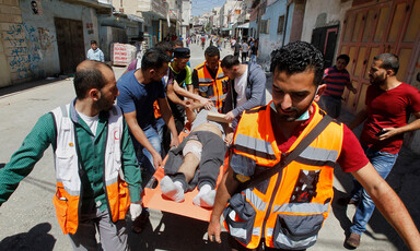 Emergency medics carry man on stretcher with protesters in background