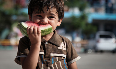 A smiling young boy eats a slice of watermelon