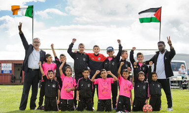 Boys in football jerseys pose with their fists in the air in front of the flags of Ireland and Palestine